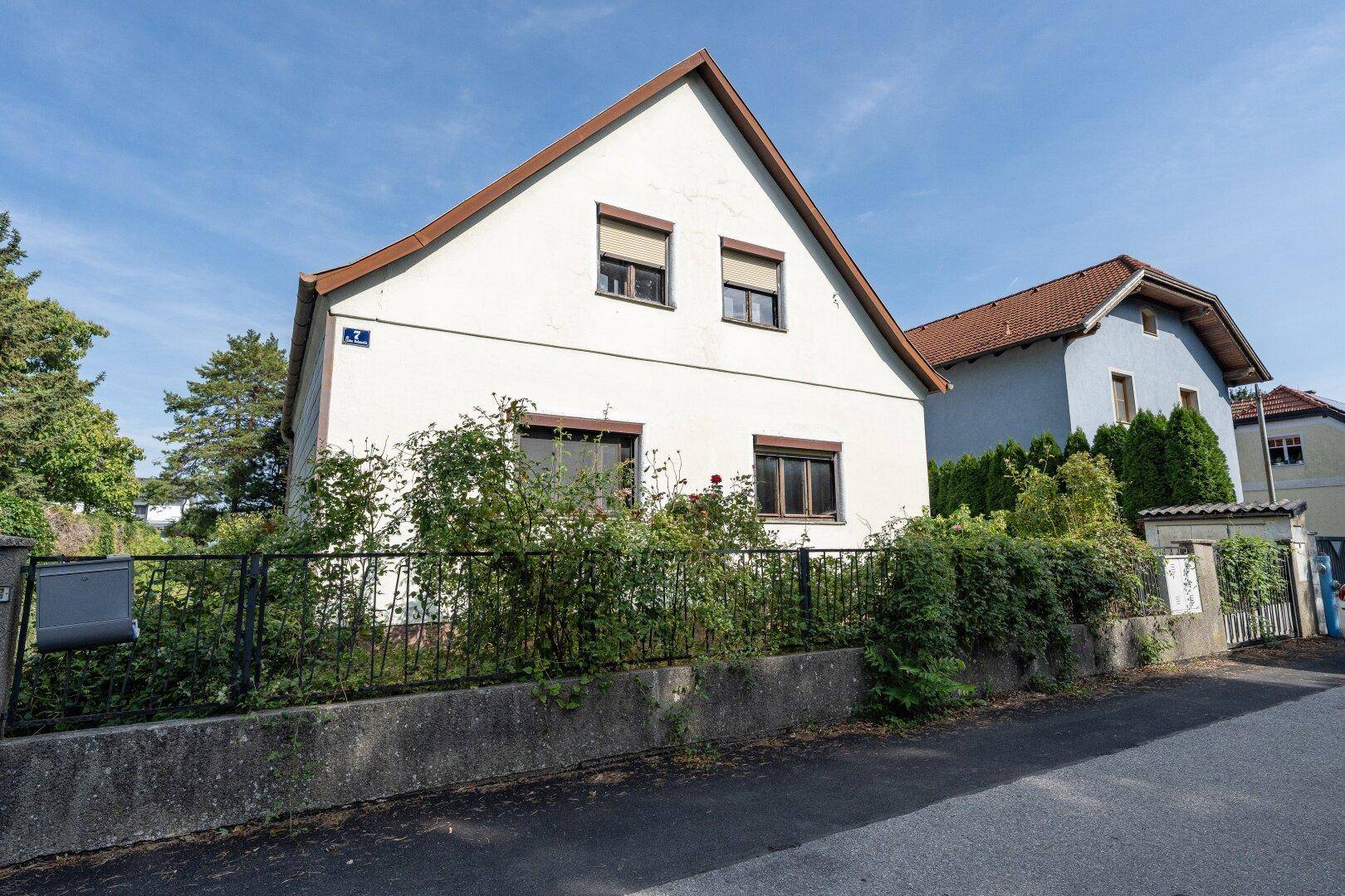 Vorderansicht des Hauses von der Straße aus mit Fenstern, Rollläden und einem Gartenzaun.