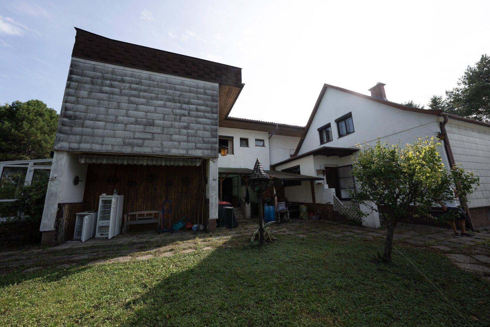 Rückansicht eines Hauses mit Gartenbereich und schrägen Dächern unter blauem Himmel.