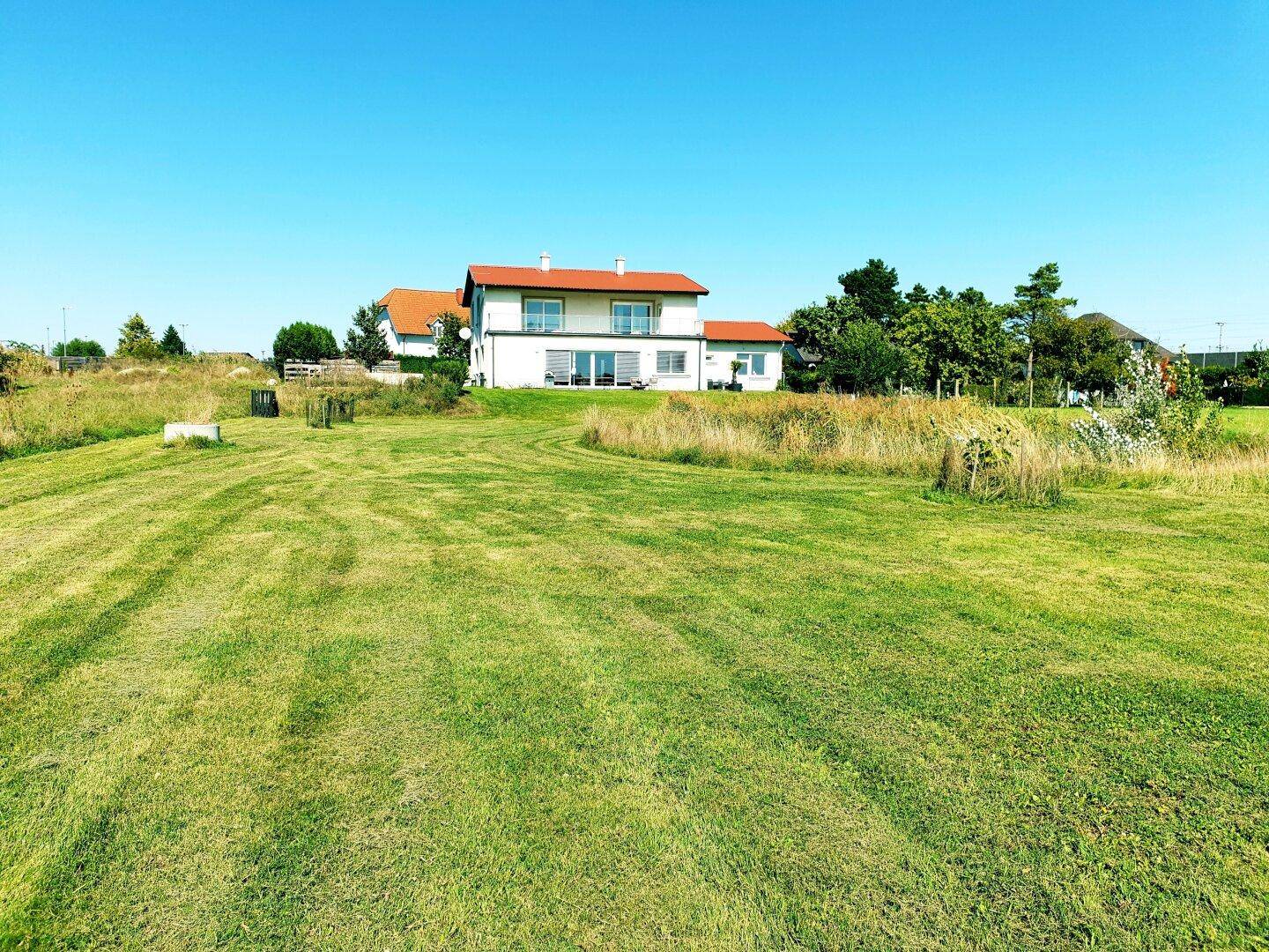 Freistehendes Einfamilienhaus mit rotem Dach und weitläufiger Grünfläche unter blauem Himmel.