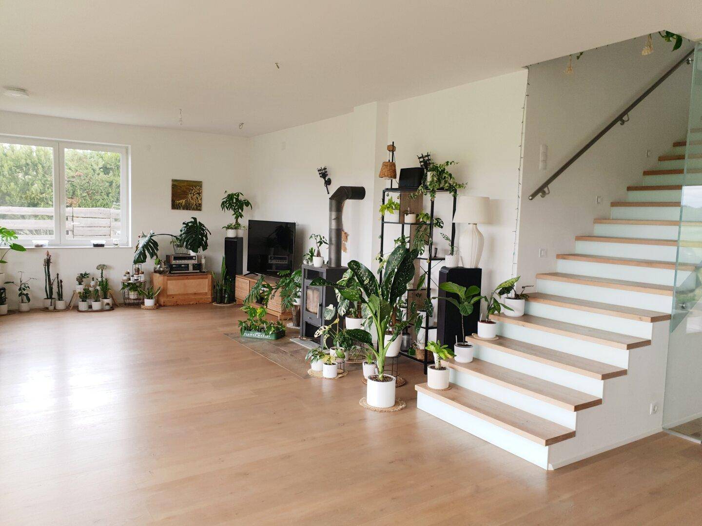 Helles Wohnzimmer mit Holzboden, modernem Kaminofen und offener Treppe mit Glasgeländer.