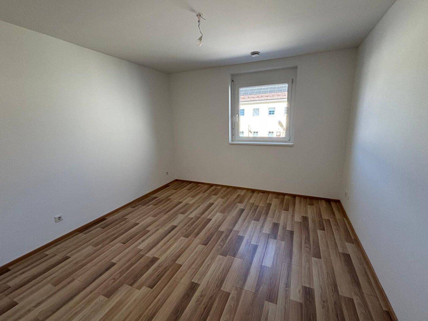 Leeres Zimmer mit Laminatboden und einem Fenster, das für natürliche Belichtung sorgt.