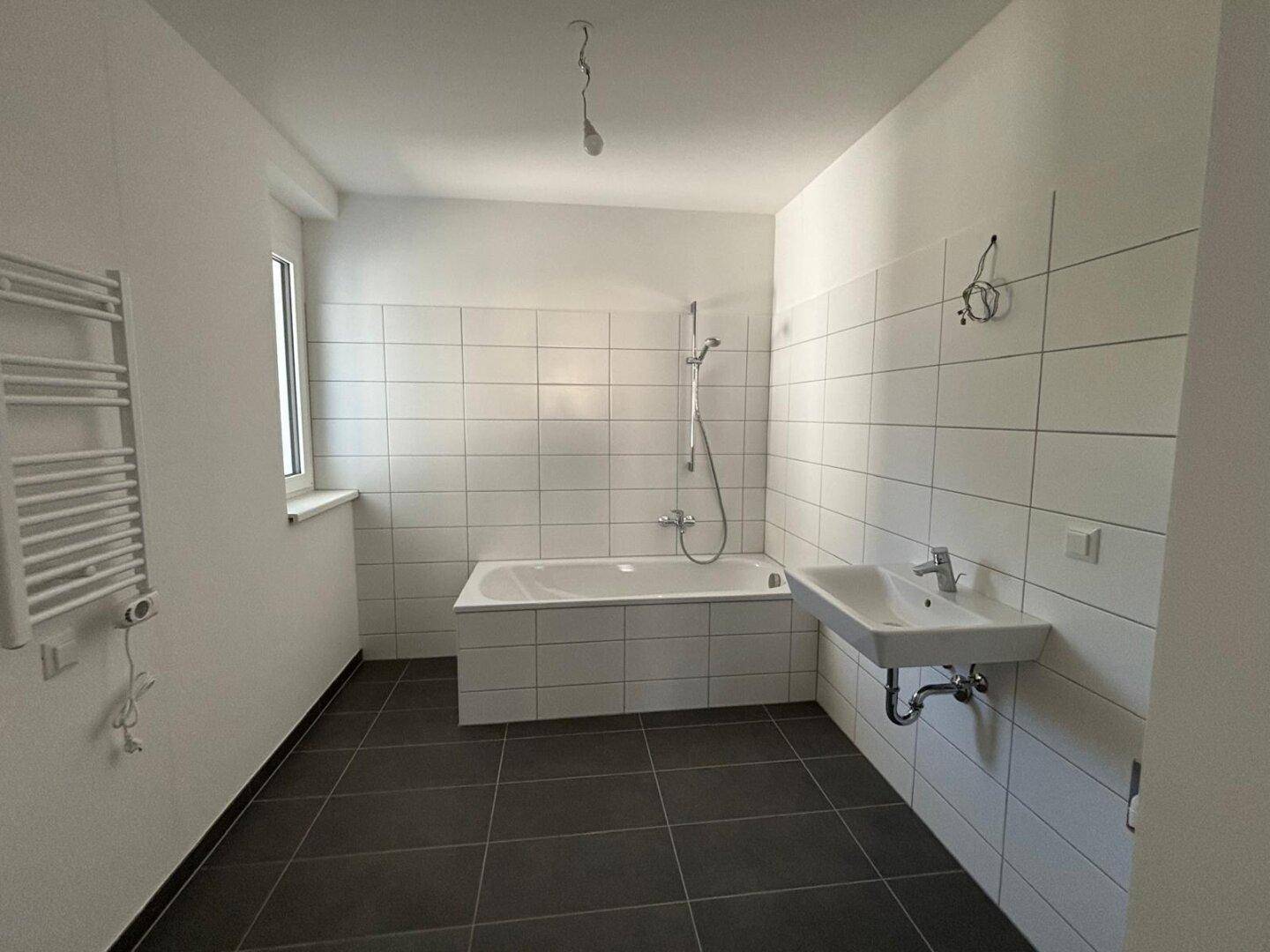 Modernes Badezimmer mit weißen Fliesen, Badewanne, Waschbecken und beheiztem Handtuchhalter.