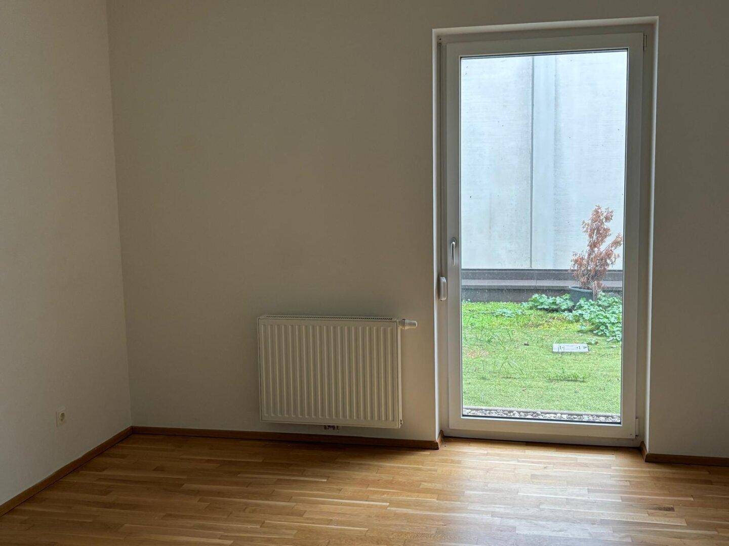 Heller Raum mit Holzboden und direktem Zugang zu einem kleinen Gartenbereich.