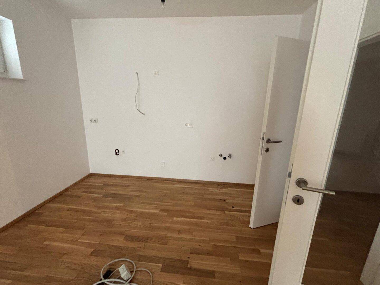 Leeres Zimmer mit Holzboden und weißen Wänden, bereit für individuelle Gestaltung.