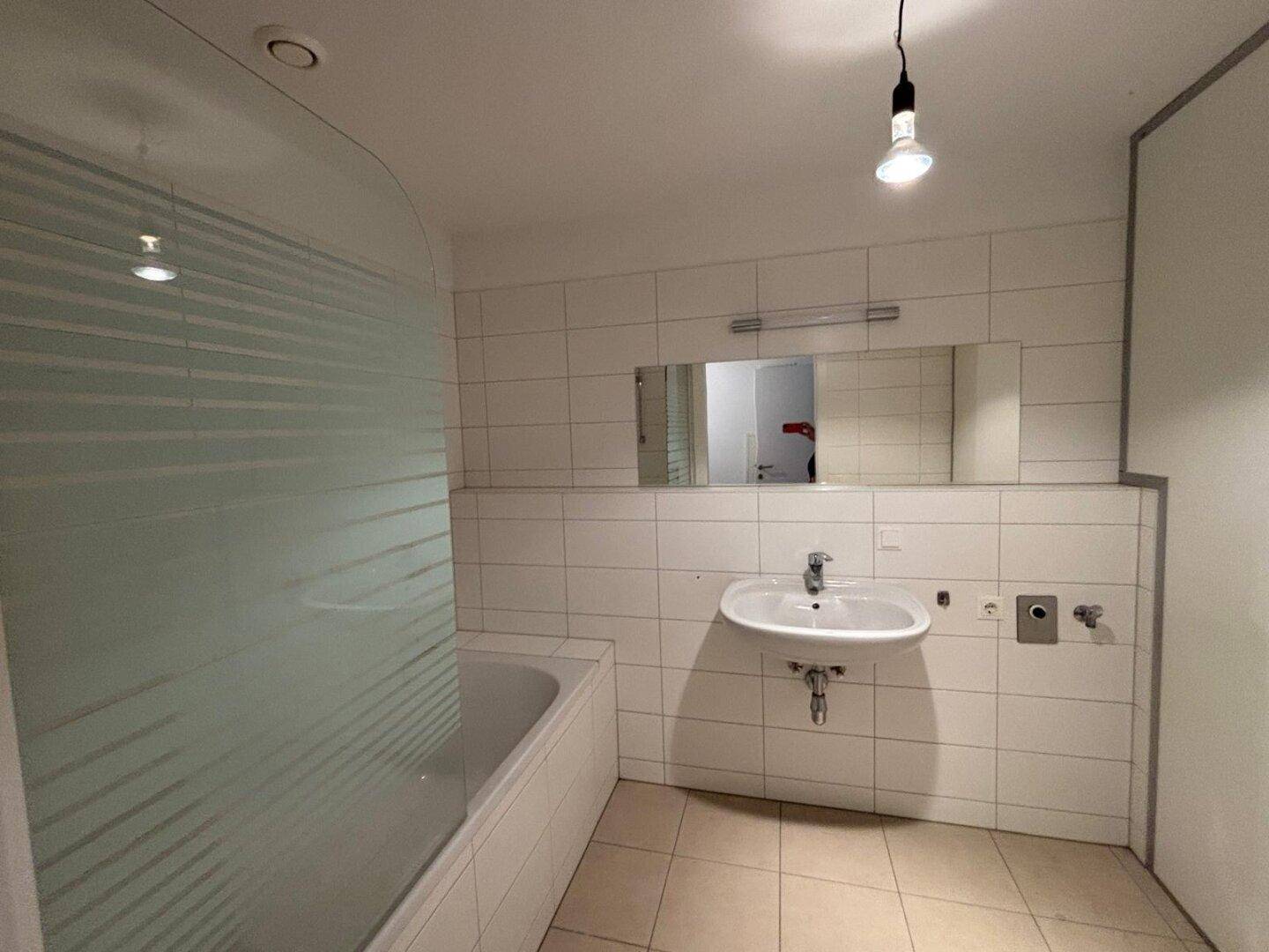 Modernes Badezimmer mit Badewanne, Waschbecken und weißen Fliesen an den Wänden.