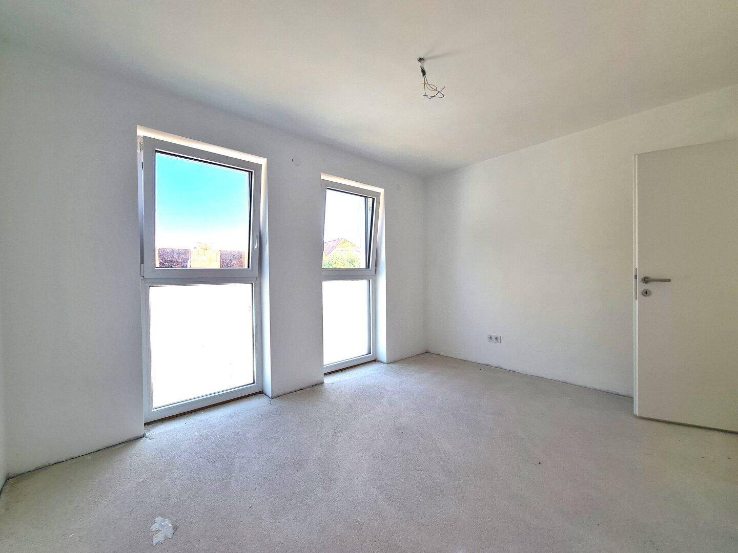 Unmöbliertes Schlafzimmer mit zwei hohen Fenstern und viel natürlichem Licht.