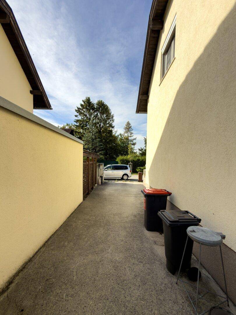 Schmaler Zugangsweg zwischen zwei Häusern mit Blick auf ein geparktes Fahrzeug.