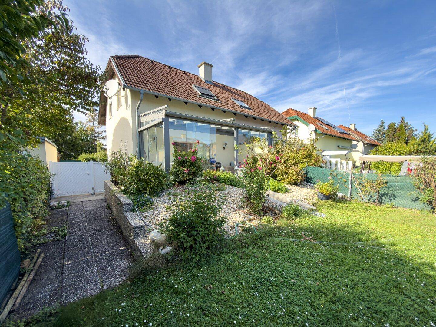 Rückansicht des Hauses mit Garten, verglaster Terrasse und gepflegter Grünfläche.