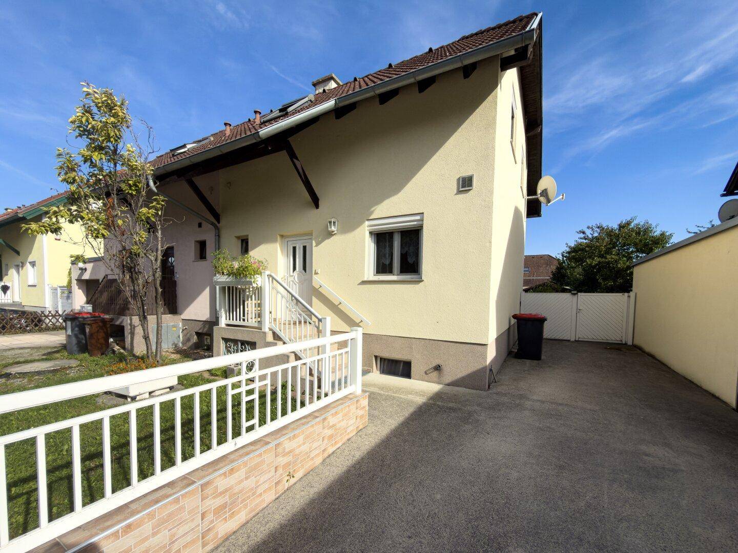 Seitenansicht des Hauses mit Zufahrt und Eingangsbereich unter blauem Himmel.