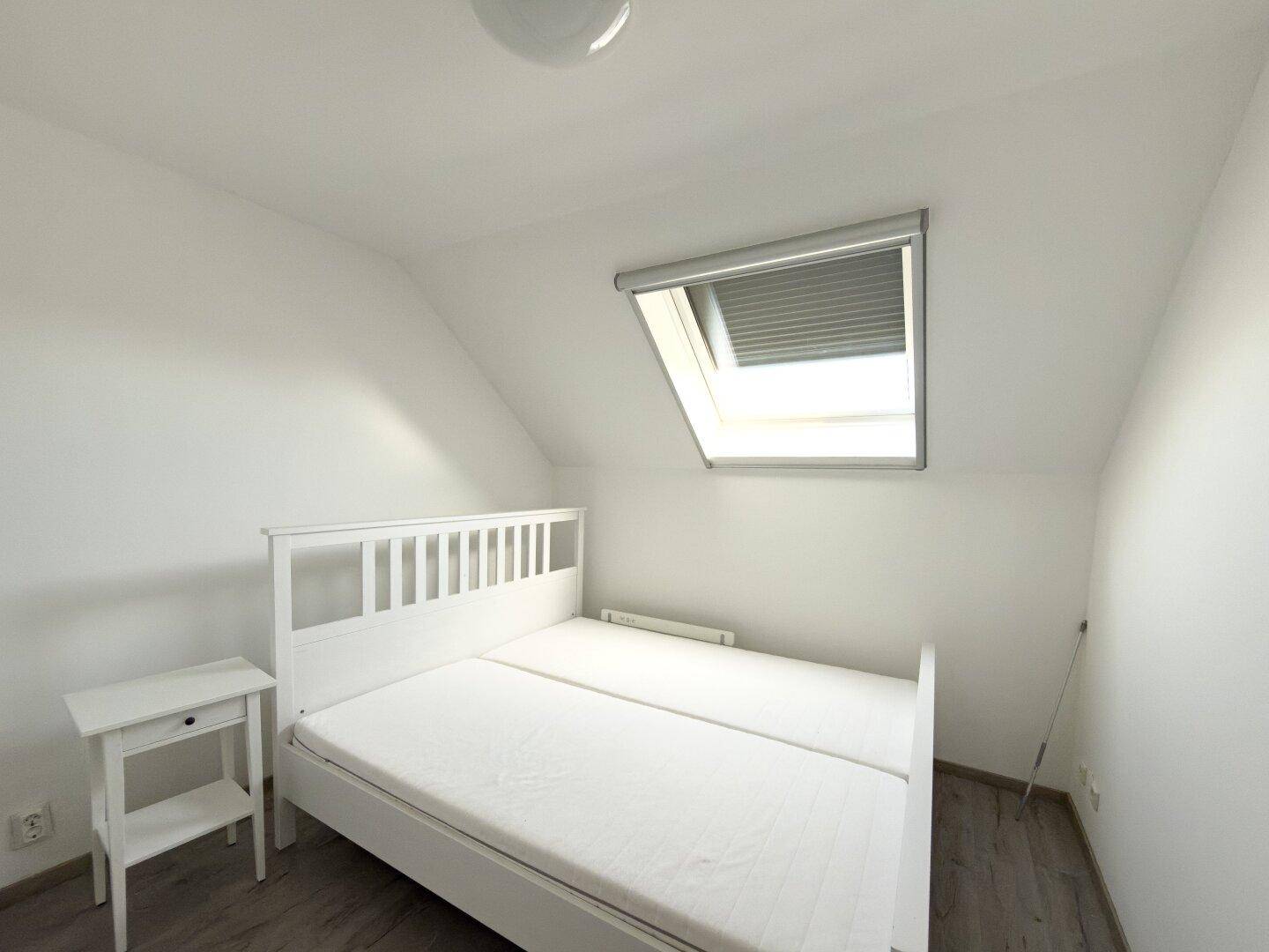 Helles Schlafzimmer im Dachgeschoss mit Dachfenster und schrägen Wänden.
