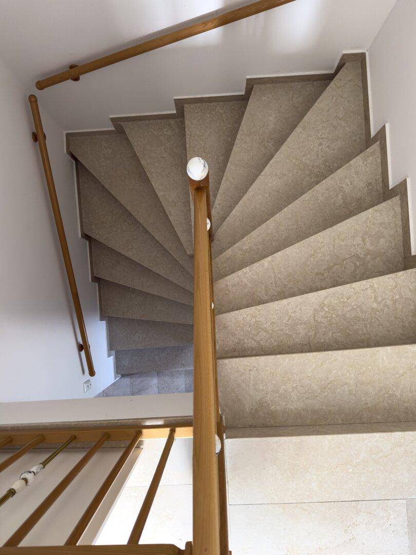 Wendeltreppe mit Holzgeländer und gefliesten Stufen, die die Stockwerke verbindet.