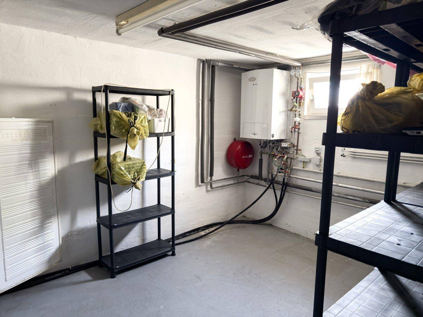 Hauswirtschaftsraum im Keller mit Regalen, Heizungsanlage und sichtbaren Leitungen.