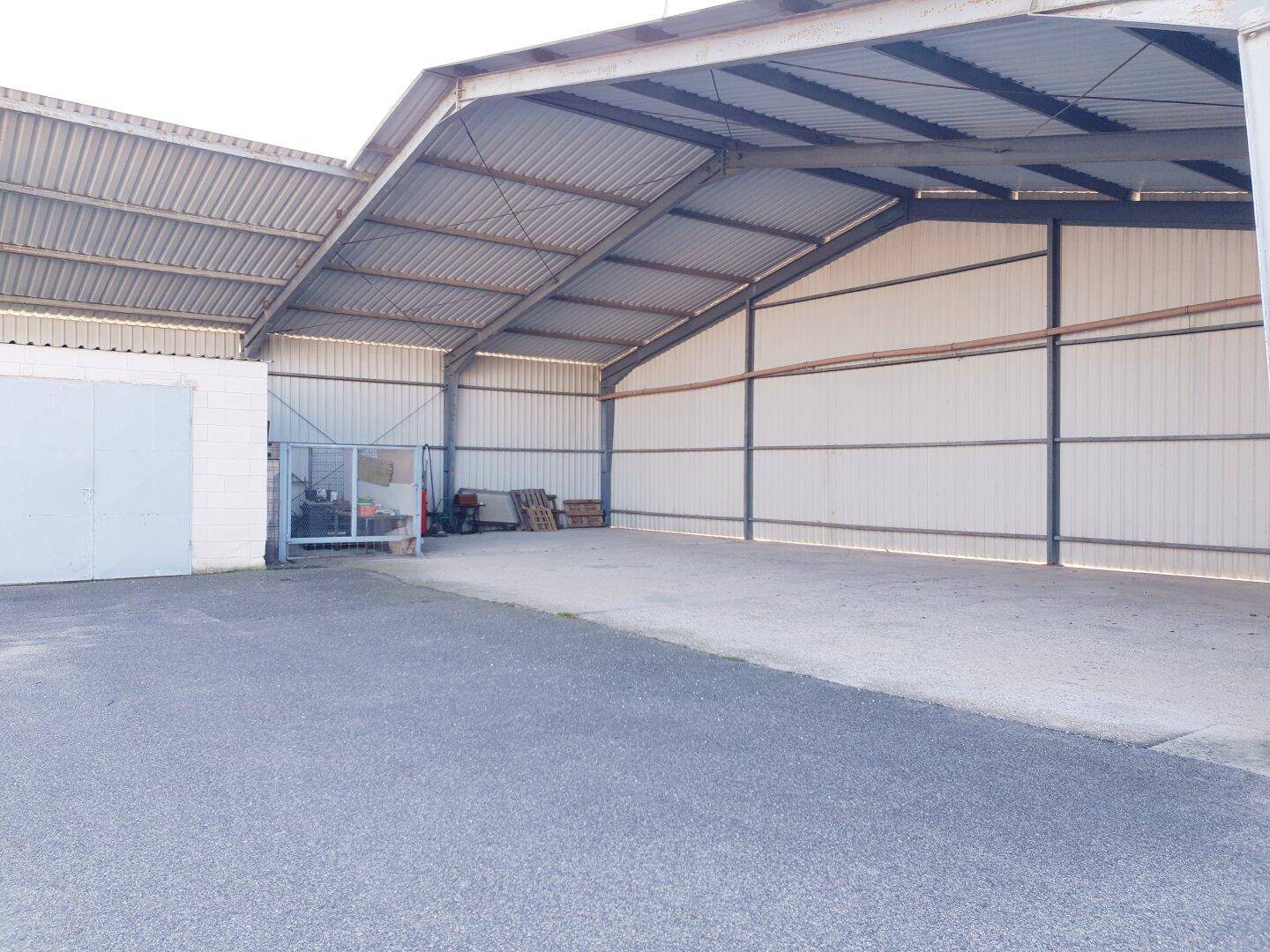 Weitläufige offene Lagerhalle mit Wellblechdach und großem asphaltierten Zufahrtsbereich.