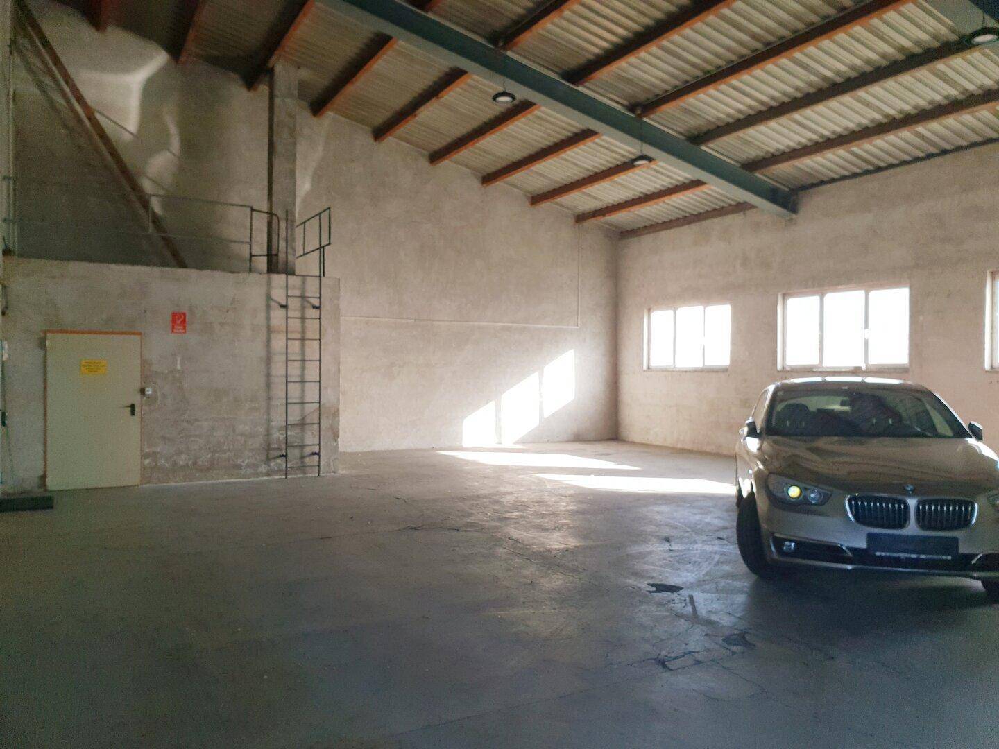 Geräumige Lagerhalle mit Betonboden, hohen Decken und einem geparkten Auto.