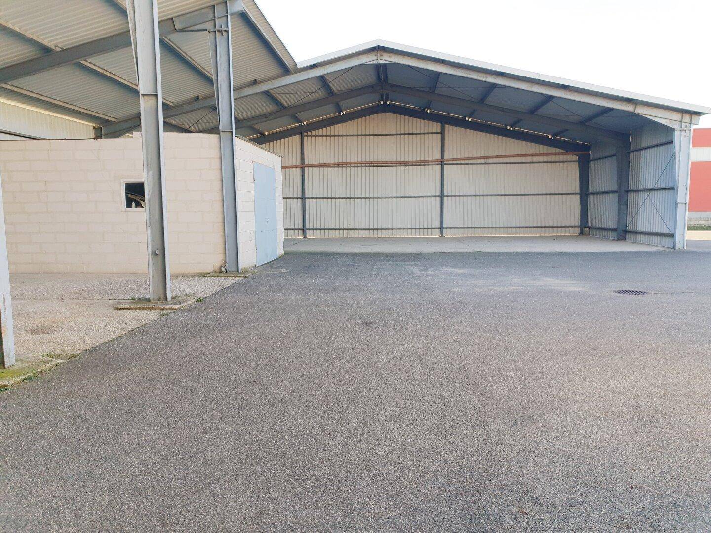 Offene Lagerhalle mit Wellblechdach und Metallkonstruktion, angrenzend an einen asphaltierten Bereich.
