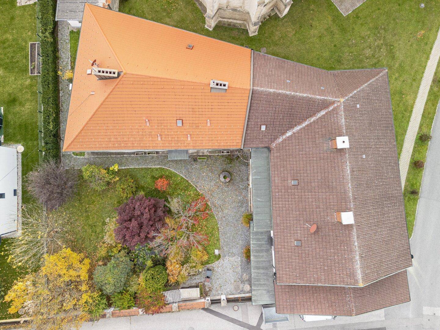 Draufsicht auf das Anwesen mit gepflastertem Innenhof und einem großen, grünen Gartenbereich.