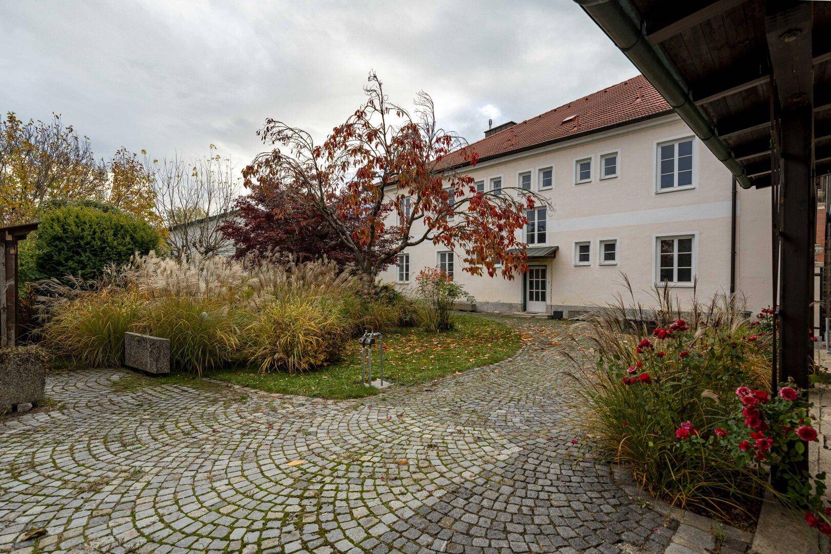 Gepflasterter Innenhof mit üppiger Bepflanzung und Blick auf die helle Fassade des Gebäudes.