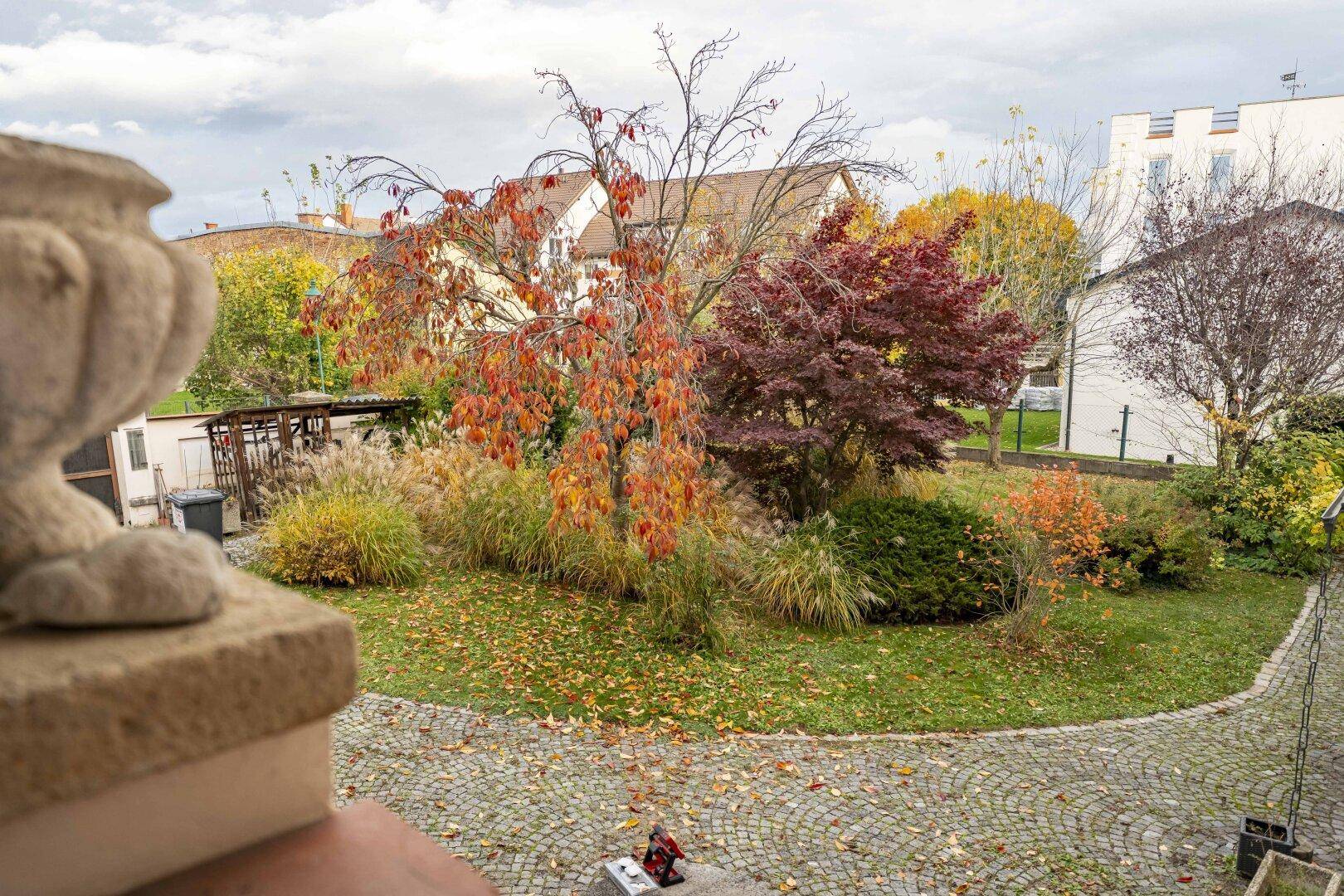 Blick von oben auf den gepflegten Garten mit Rasenfläche und bunten Herbstbäumen.