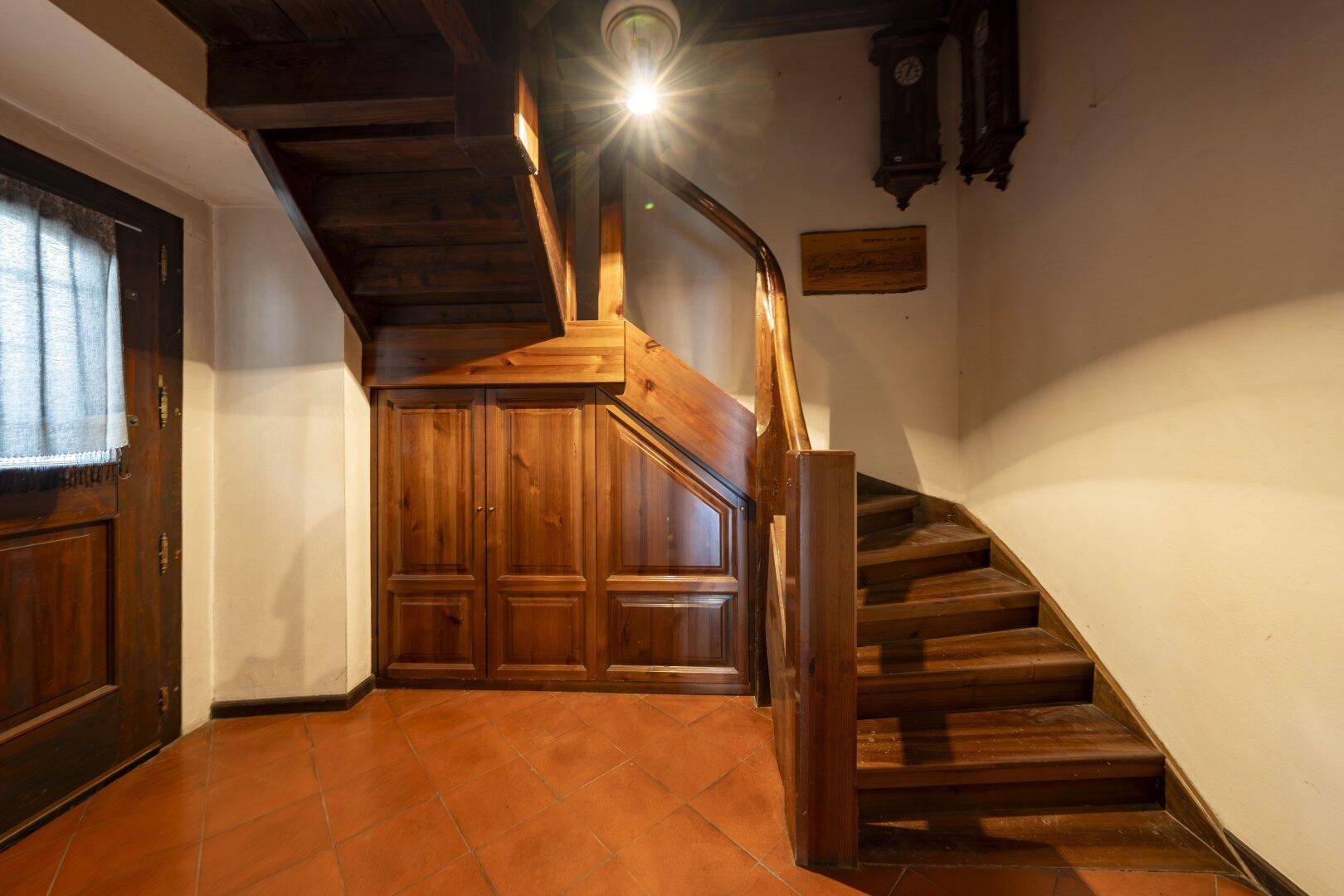 Holztreppe mit integrierten Schränken und Terrakottafliesen im Eingangsbereich.