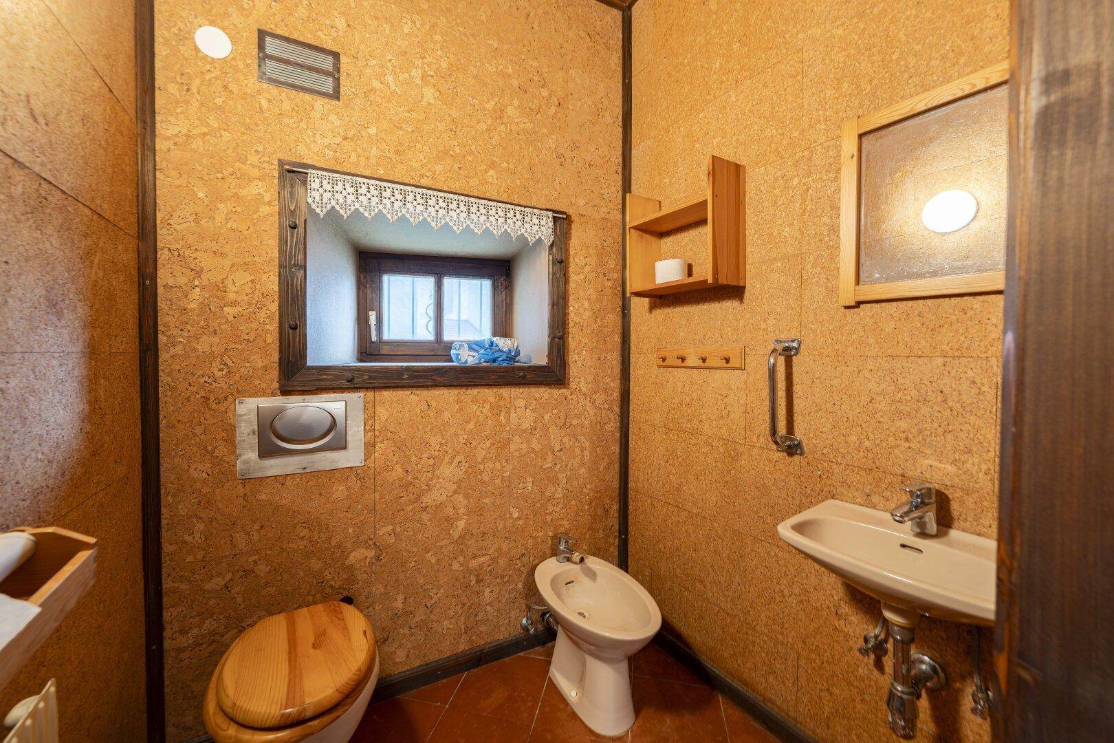 Rustikales Gäste-WC mit Korkwänden, Terrakottafliesen und einem kleinen Fenster.