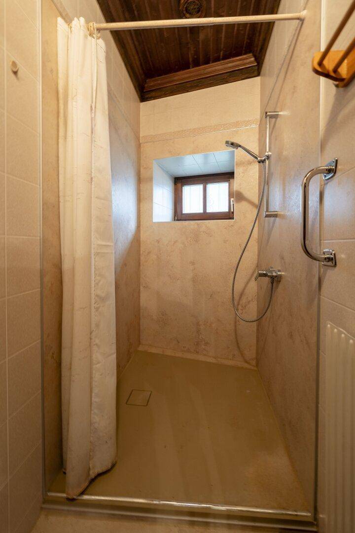 Duschbereich mit Fliesenwänden, Duschvorhang und einem kleinen Fenster.