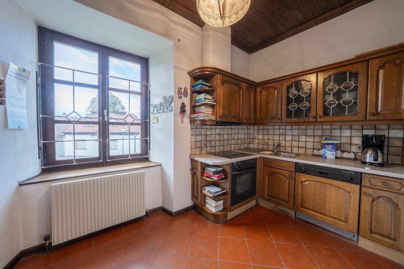 Traditionelle Holzküche mit Terrakottafliesen, Einbaugeräten und einem großen Fenster.