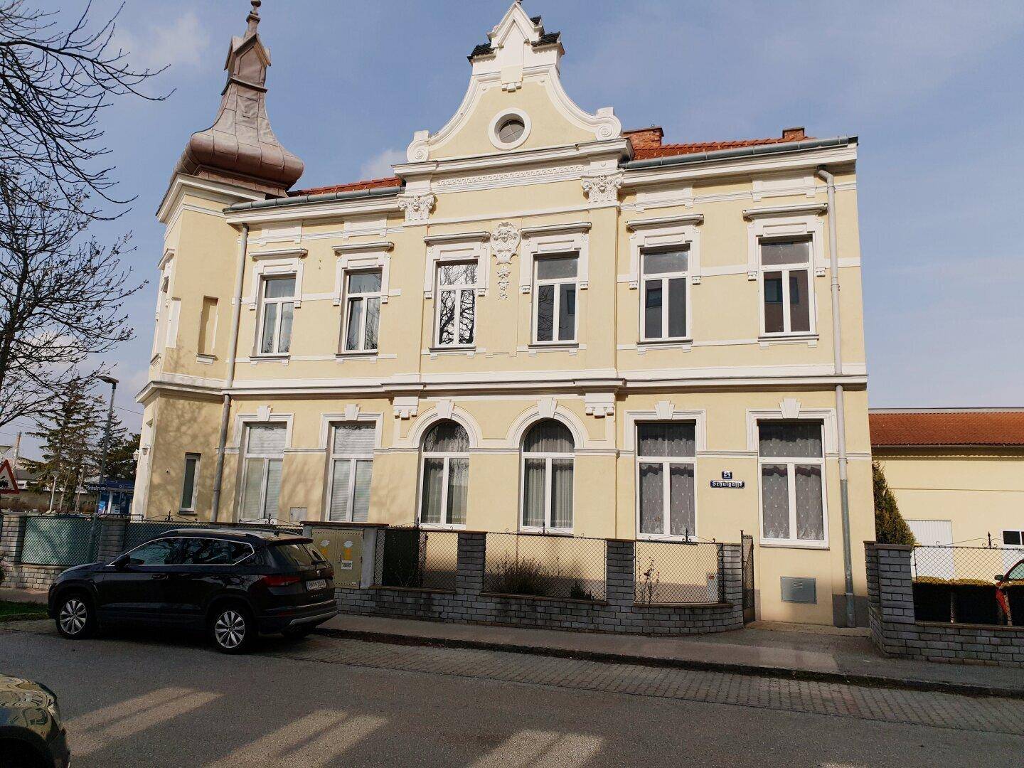 Vorderansicht des historischen Gebäudes mit gelber Fassade und dekorativen Elementen.