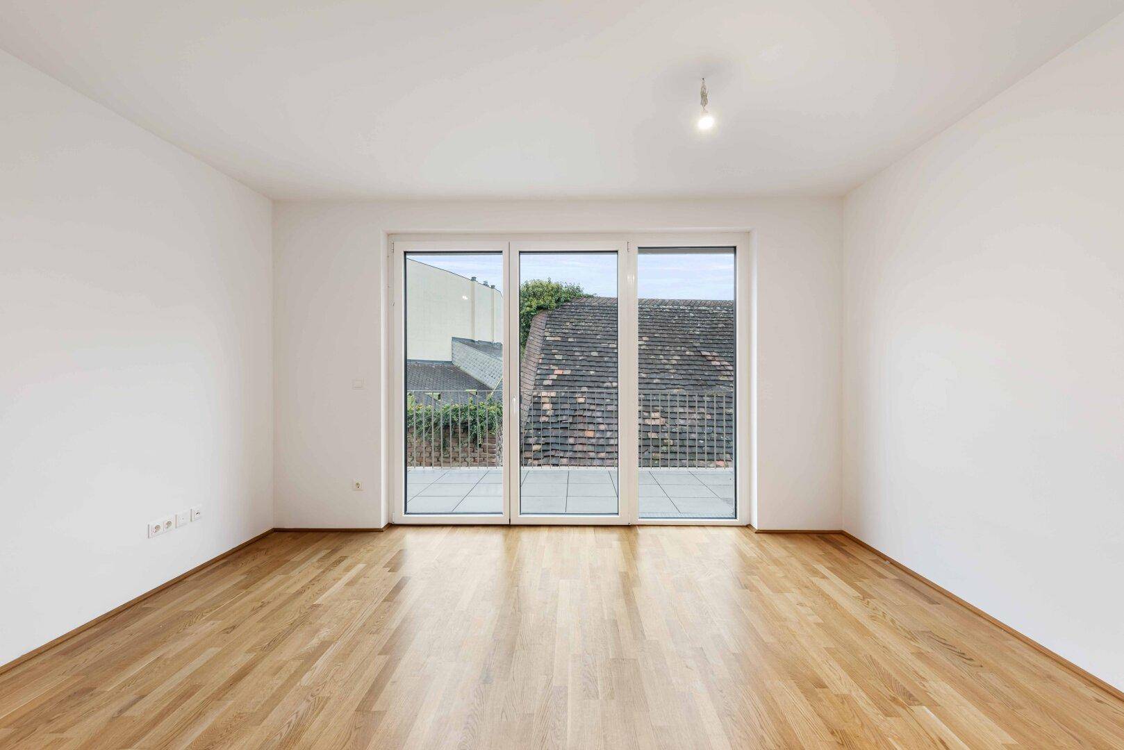 Heller Wohnraum mit Parkettboden und großen Fenstern, die Zugang zu einer Terrasse bieten.