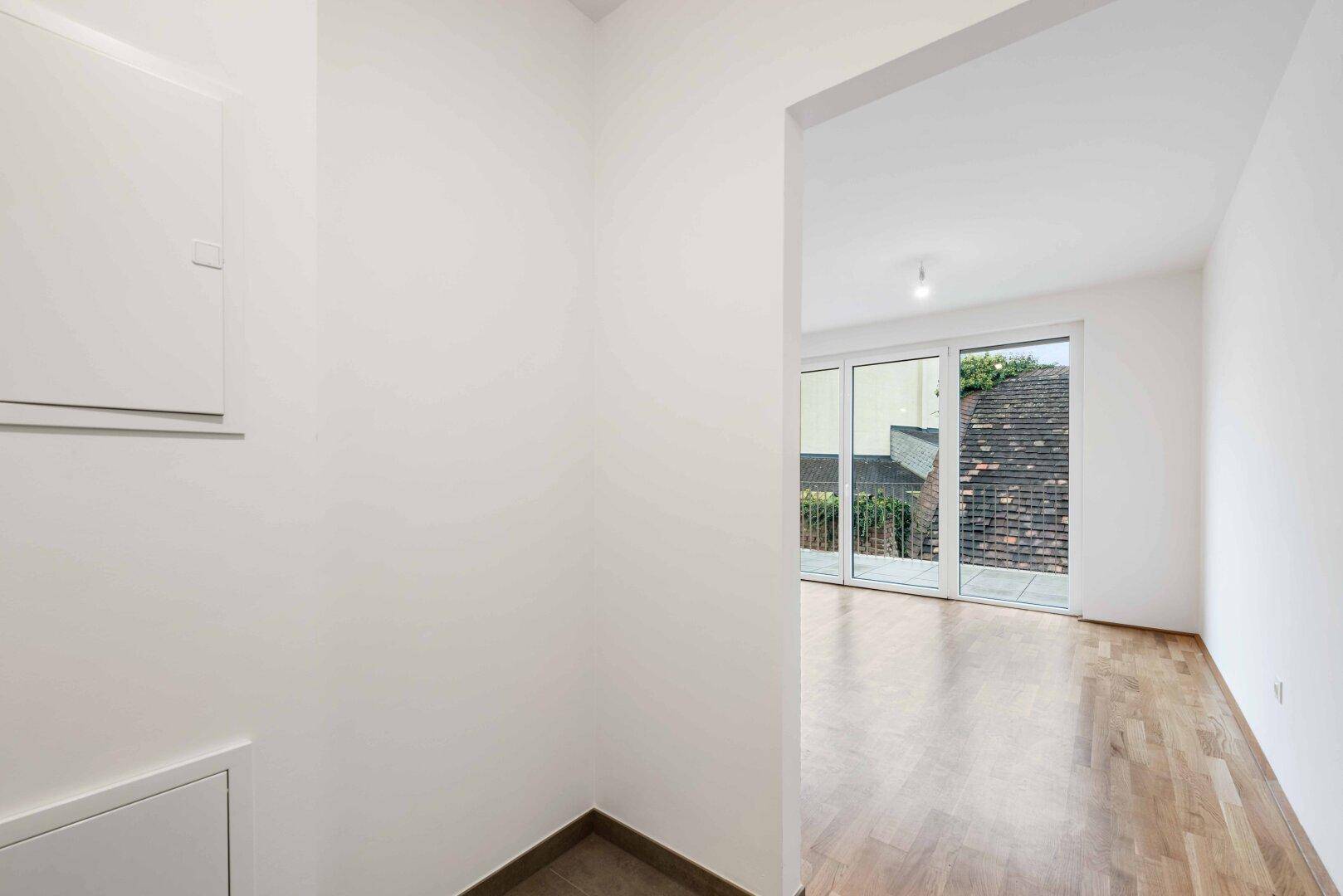 Eingangsbereich mit hellem Parkettboden und Blick in einen angrenzenden Raum mit Terrassenzugang.