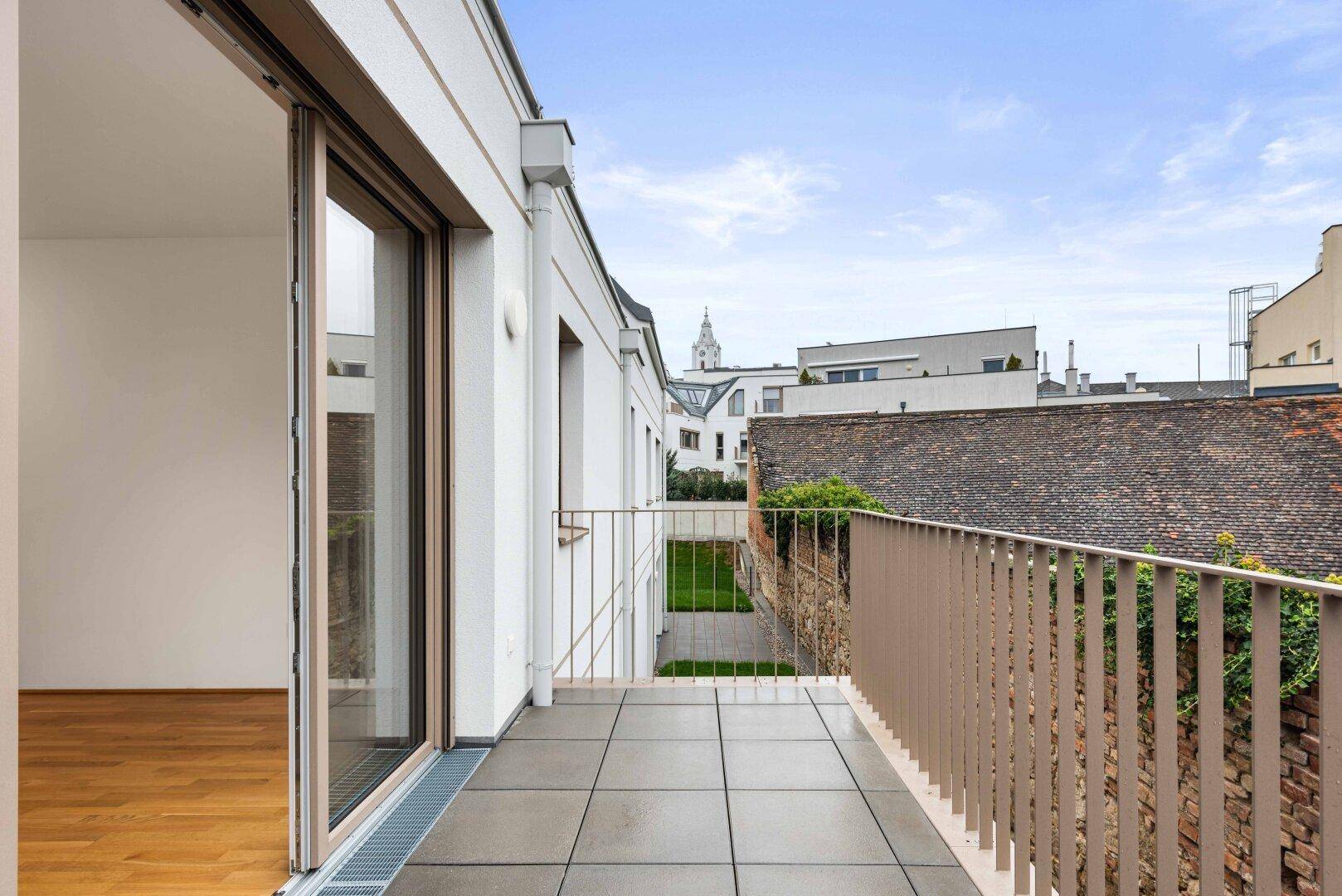 Geräumiger Balkon mit Fliesenboden und Blick auf die umliegenden Gebäude und den Himmel.