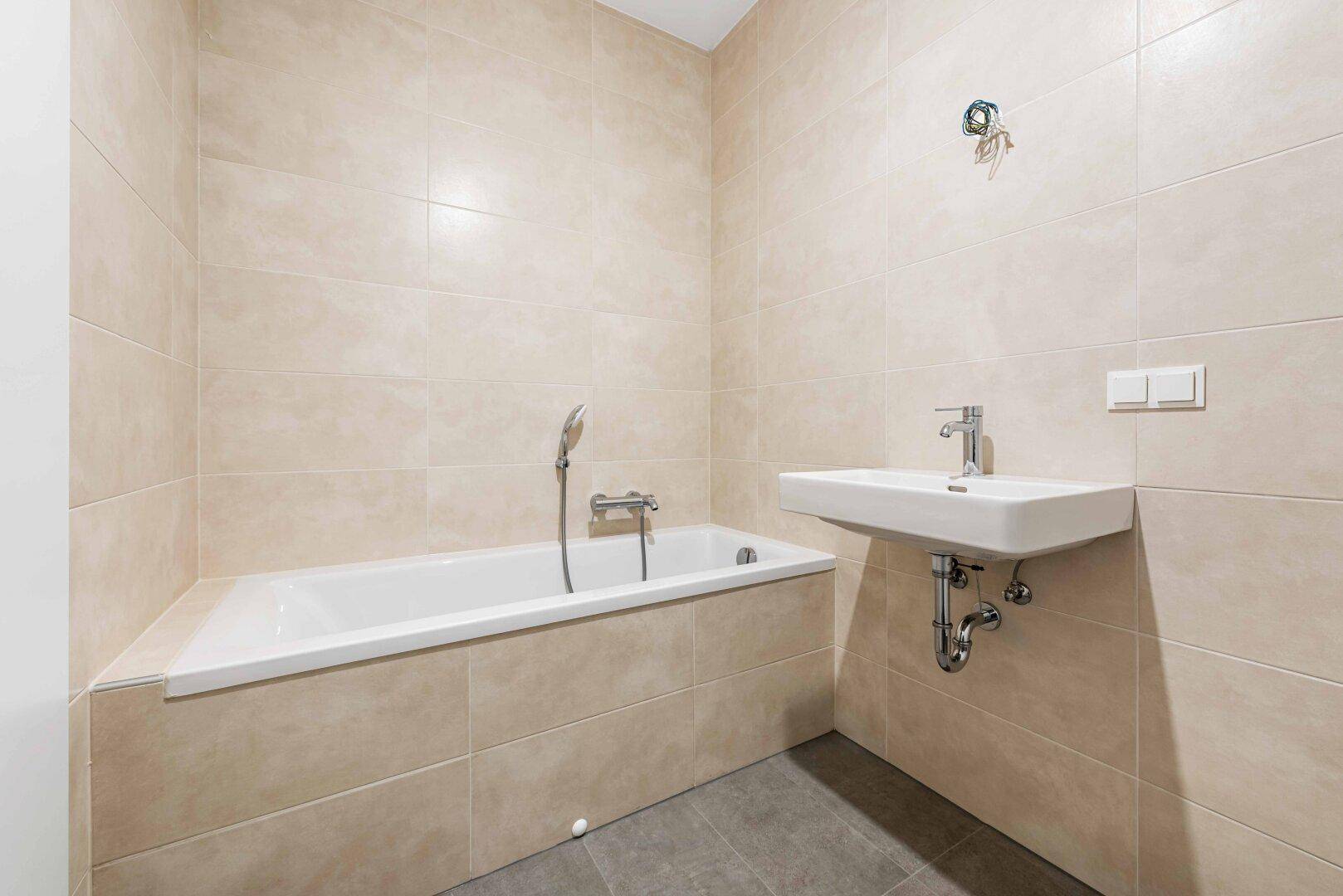 Modernes Badezimmer mit beigefarbenen Fliesen, Badewanne und Waschbecken.