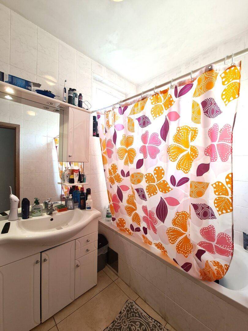 Badezimmer mit Badewanne, farbenfrohem Duschvorhang, Einzelwaschbecken und Spiegelschrank.