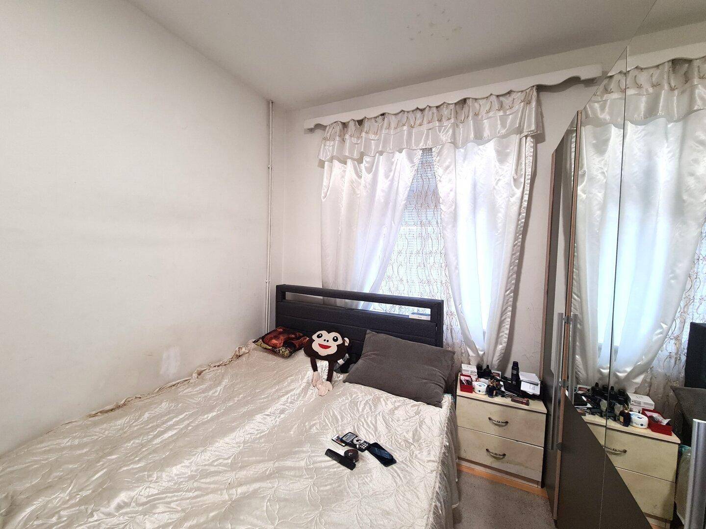 Kleines Schlafzimmer mit Einzelbett, Spiegelschrank und Vorhängen am Fenster.