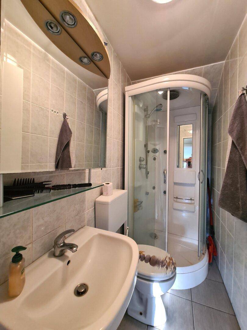 Kleines Badezimmer mit Duschkabine, WC und Einzelwaschbecken, hell gefliest.