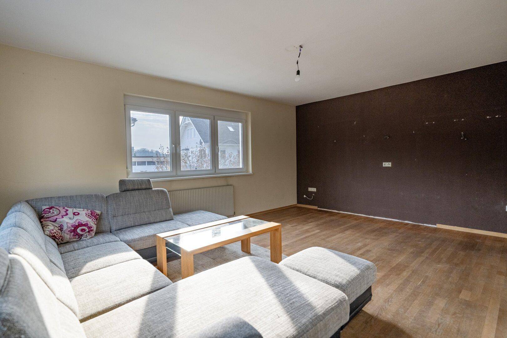 Wohnzimmer mit Holzboden und einer dunklen Akzentwand, bietet viel Platz für individuelle Gestaltung.