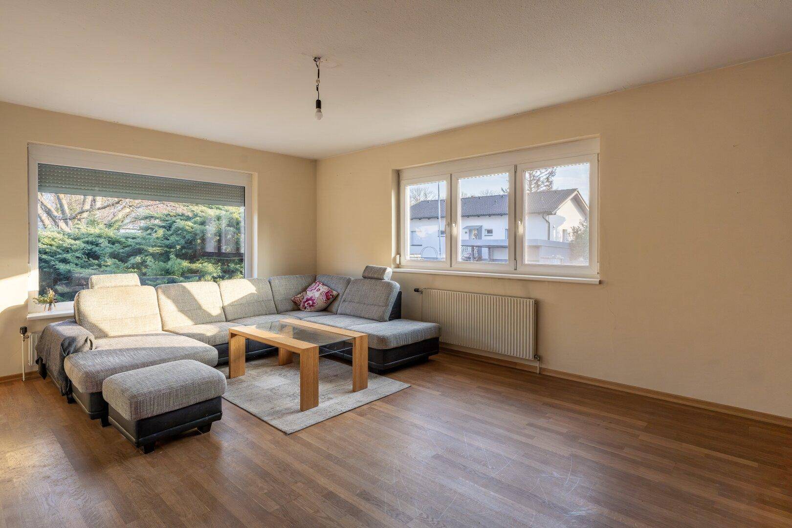 Geräumiges Wohnzimmer mit Holzboden, großem Ecksofa und Fenstern mit Blick ins Grüne.
