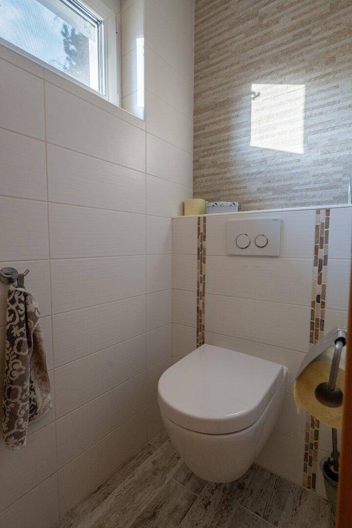 Gäste-WC mit wandhängender Toilette, modernen Fliesen und einem kleinen Fenster für Tageslicht.