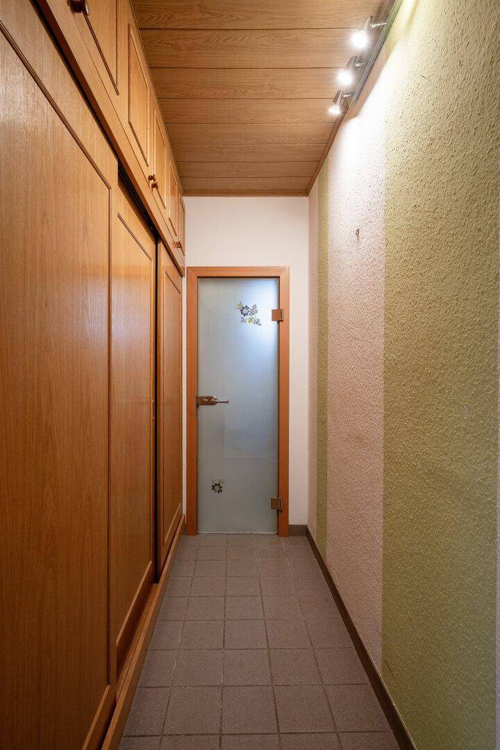 Schmaler Flur mit Einbauschränken aus Holz und einer Milchglastür am Ende des Ganges.