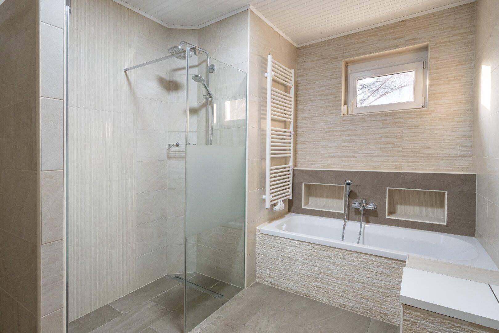 Modernes Badezimmer mit begehbarer Dusche, Badewanne und beheiztem Handtuchhalter in hellen Tönen.