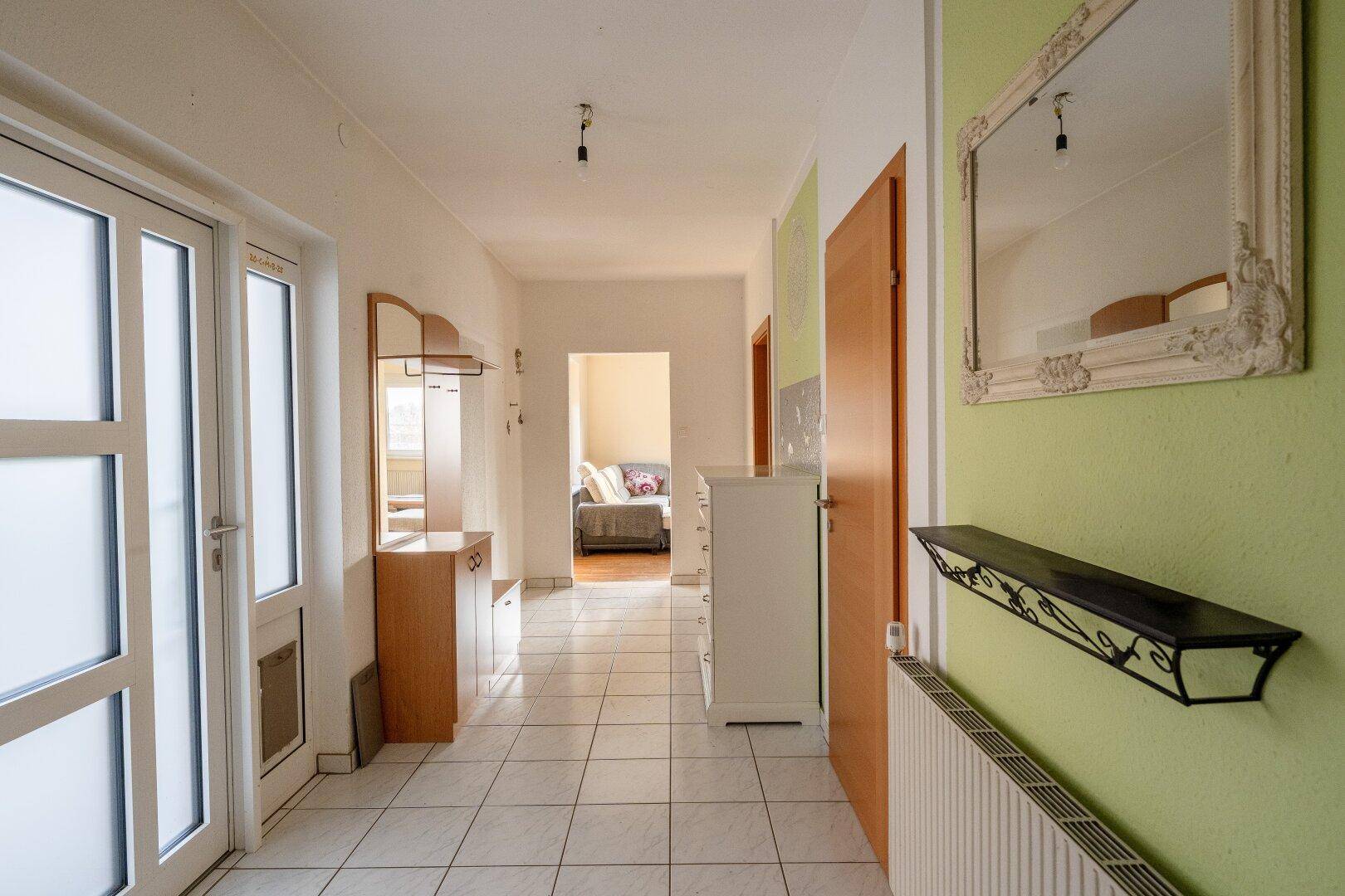 Heller Flur mit Fliesenboden, Garderobe und einem Spiegel, der zu weiteren Räumen führt.