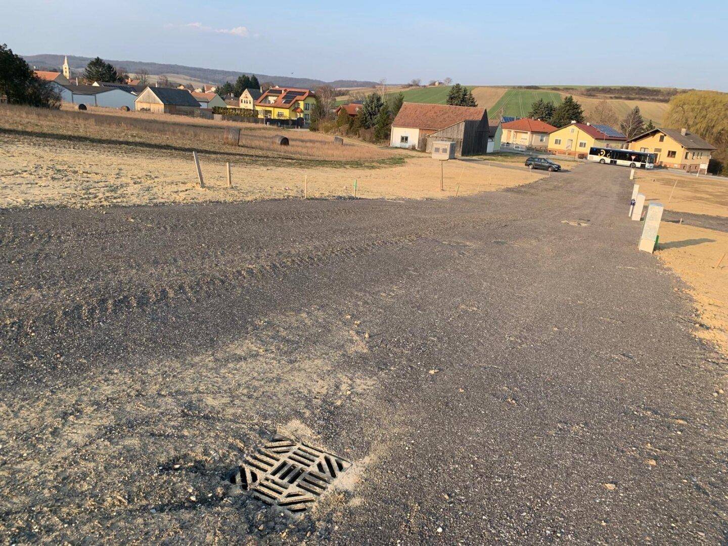 Baureifes Grundstück mit Entwässerungsrinne und Fernblick auf ein Dorf in der Hügellandschaft.