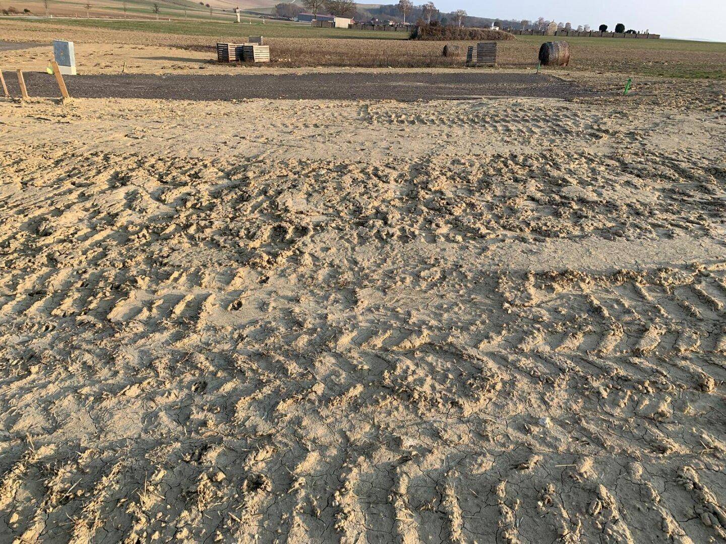 Aufgewühlter Erdboden mit tiefen Reifenspuren, möglicherweise von Baufahrzeugen, auf einem Grundstück.