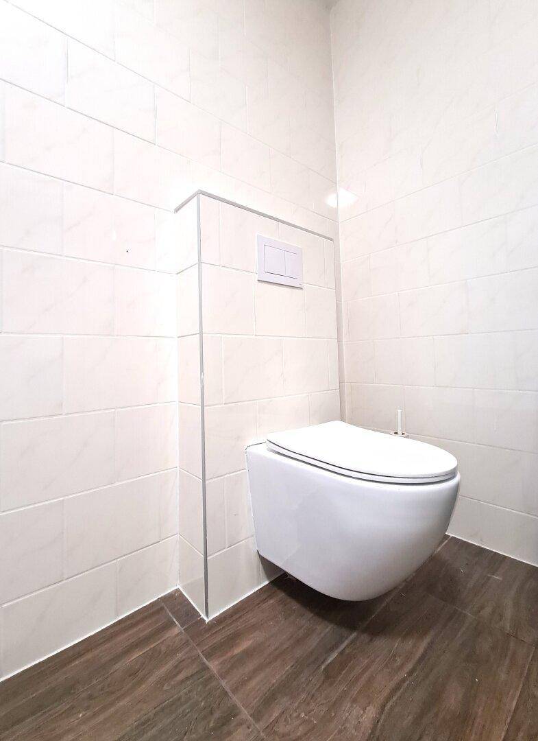 Separate Toilette mit wandmontiertem WC und weißen Fliesen.