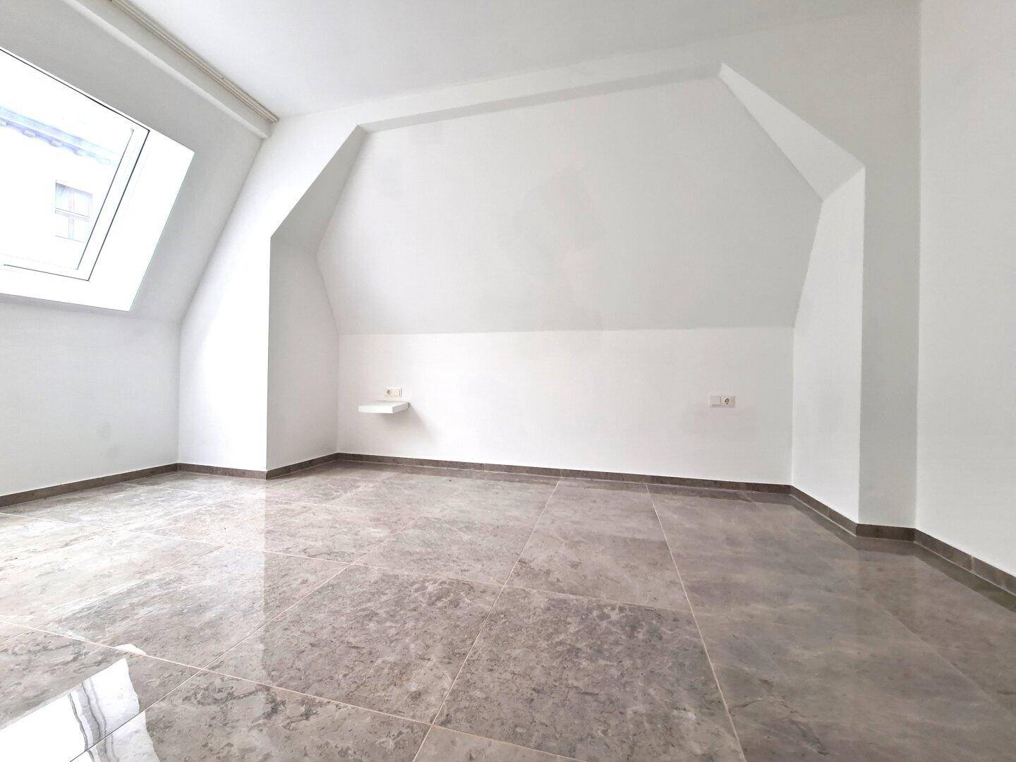 Leerer Raum mit schrägen Wänden, Dachfenster und glänzenden Fliesen.