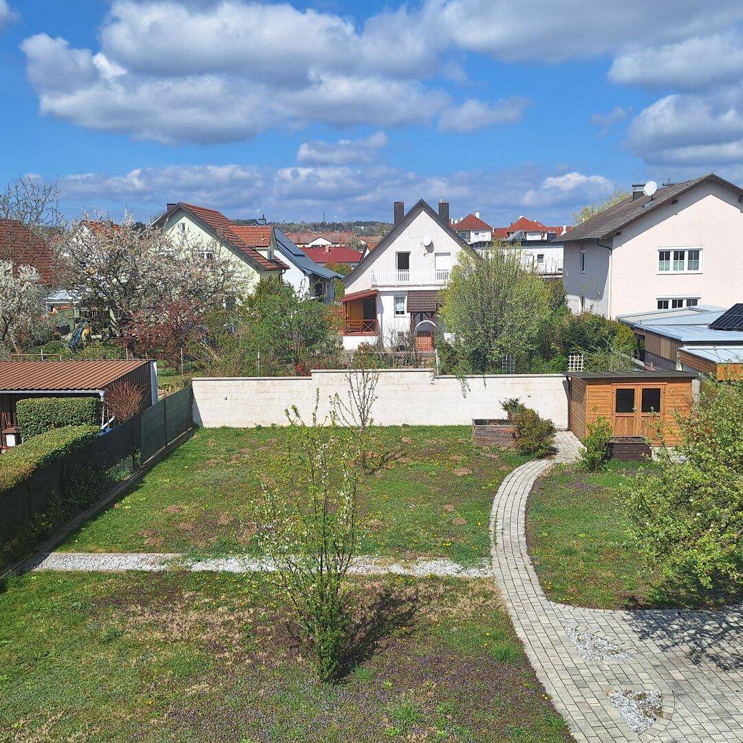 Großer Garten mit Rasenfläche, gepflastertem Weg und Gartenhaus, umgeben von weiteren Wohnhäusern.