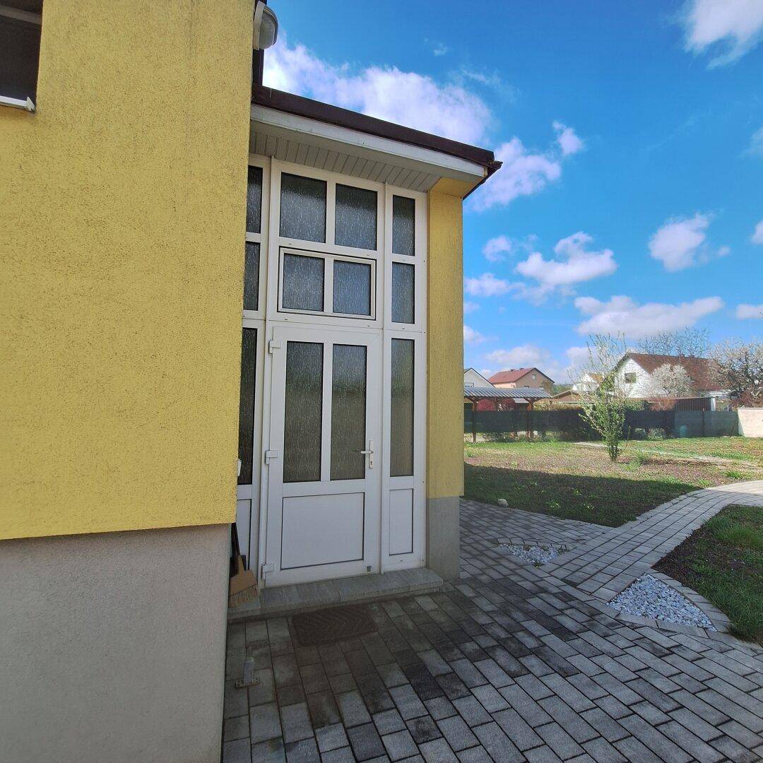 Seitlicher Eingangsbereich des Hauses mit gepflastertem Zugang und Blick auf den Garten.
