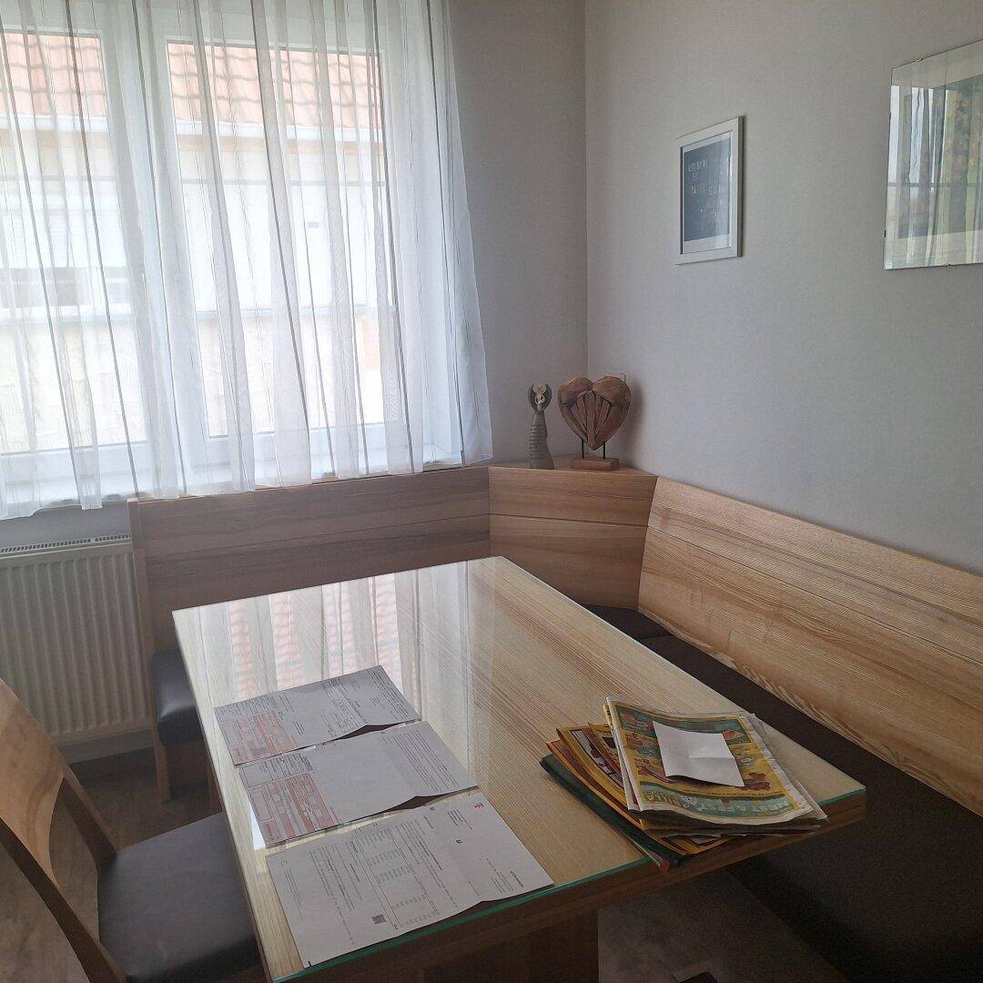 Gemütlicher Essbereich mit Eckbank, Holztisch und Fenster mit Vorhängen.
