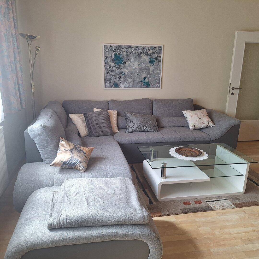 Gemütliches Wohnzimmer mit Ecksofa, Couchtisch und Teppichboden.