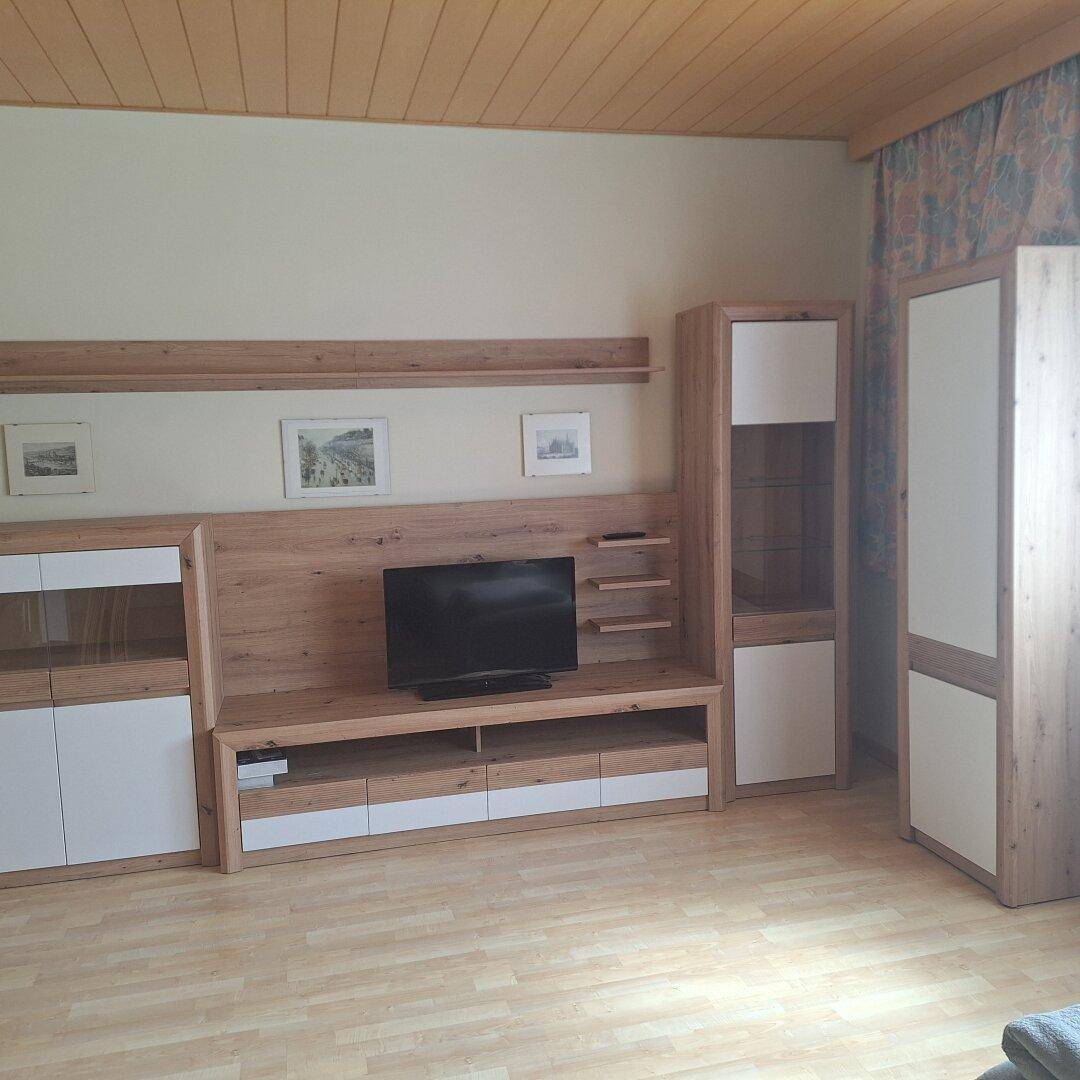 Wohnzimmer mit moderner TV-Wand, Holzdecke und hellem Laminatboden.