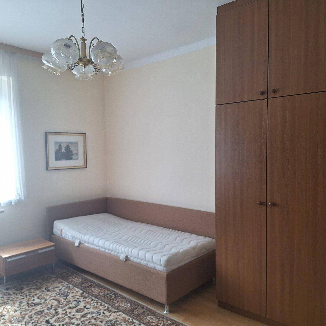 Schlafzimmer mit Einzelbett, Kleiderschrank und Teppich auf Laminatboden.